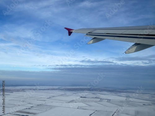 View of wing from plane window, flying above snowy fields in winter