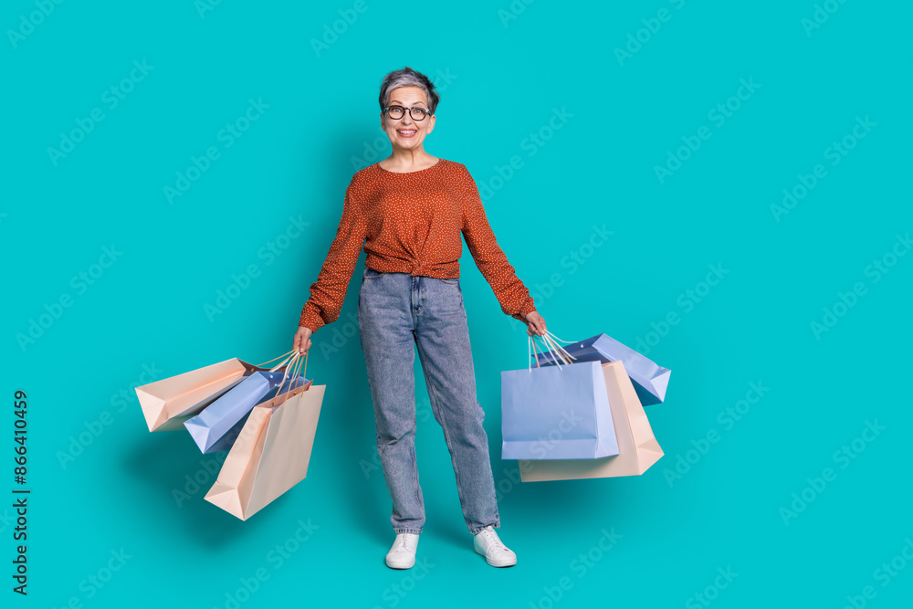 Full length photo of lovely pensioner lady shopping bags dressed stylish brown garment isolated on cyan color background Full length photo of lovely pensioner lady shopping bags dressed stylish brown garment isolated on cyan color background