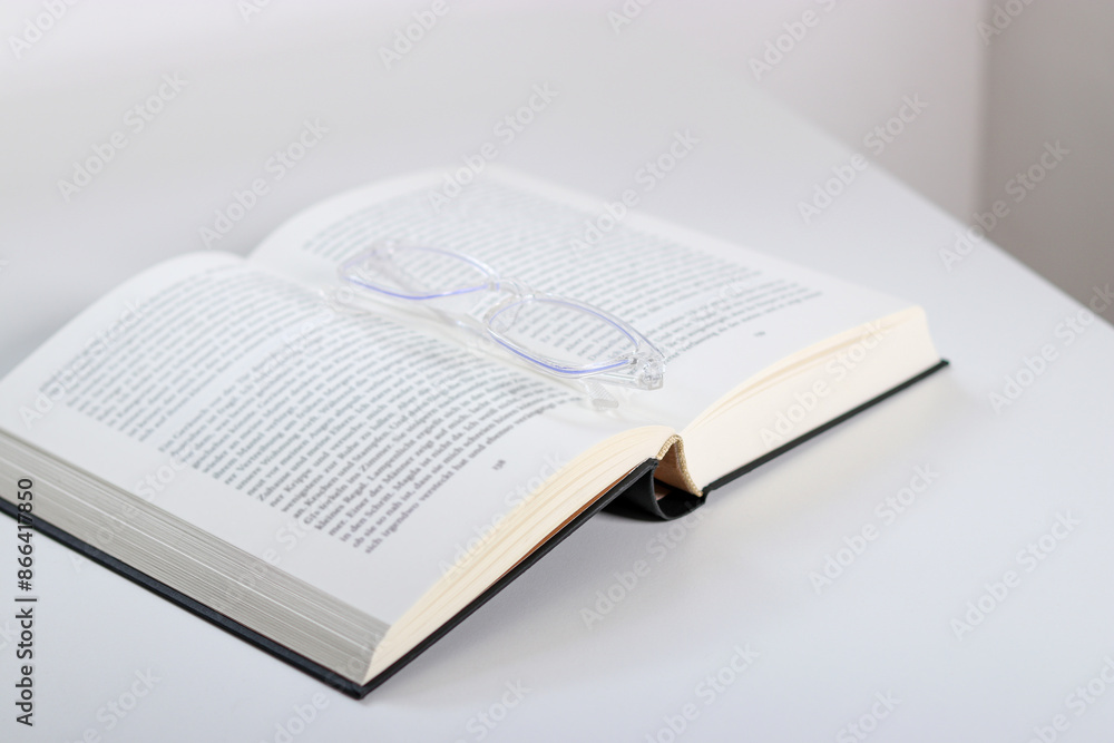 Obraz premium Close up of transparent glasses and an open book on white table 