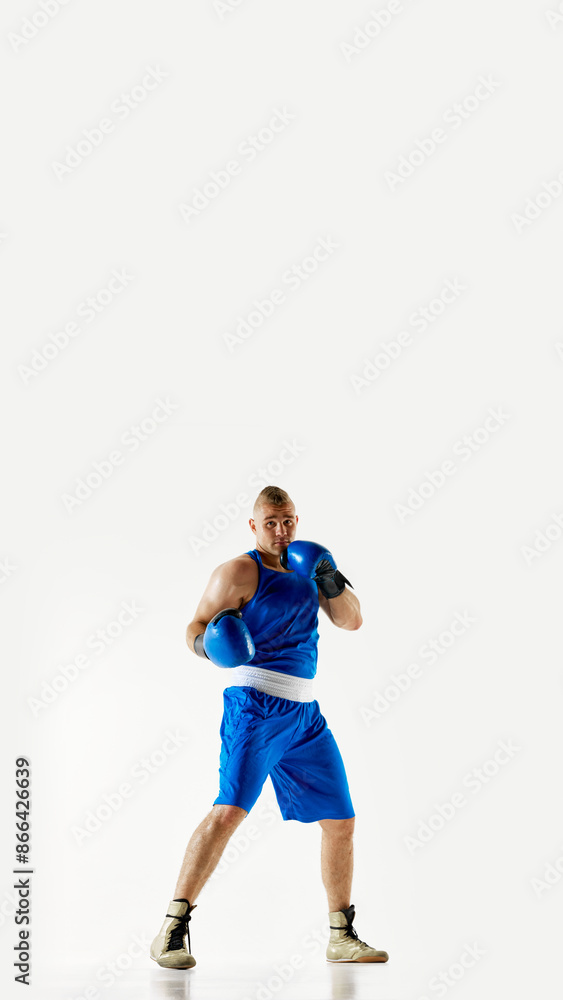 Poster. Young athletic man, focused on his footwork and timing boxer in blue uniform training against white studio background. Concept of professional combat sport, healthy lifestyle, competition. Ad Poster. Young athletic man, focused on his footwork and timing boxer in blue uniform training against white studio background. Concept of professional combat sport, healthy lifestyle, competition. Ad