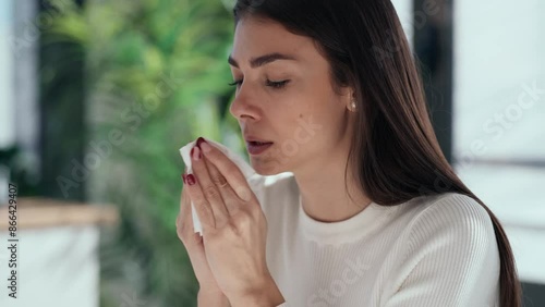Video of illness business woman sneezing in a tissue while working with computer in a modern office