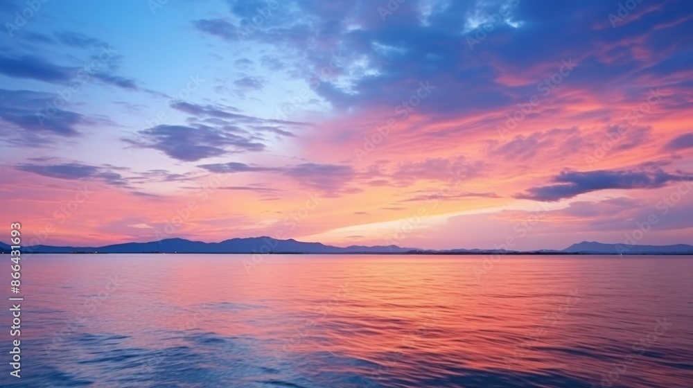 This image features a calm ocean beneath a colorful sunset sky dotted with clouds, where the warm hues of pink, purple, and blue create a tranquil and picturesque scene.