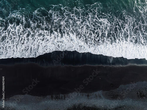 Dramatic contrast of white ocean waves crashing against the black sand beach in Iceland. Captured from above, showcasing the unique natural beauty.