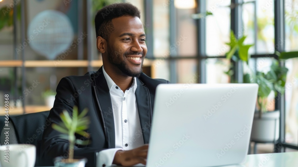 A happy Latin businessman in a black suit and white shirt is working on his laptop in an office setting. He is smiling and looks confident as he works A happy Latin businessman in a black suit and white shirt is working on his laptop in an office setting. He is smiling and looks confident as he works