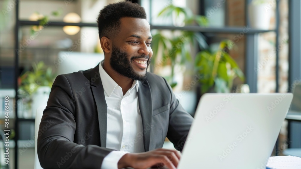 A happy Latin businessman in a suit sits at a desk in a modern office, smiling as he works on his laptop A happy Latin businessman in a suit sits at a desk in a modern office, smiling as he works on his laptop