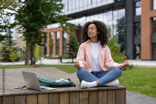 Canvas Print Young female student practicing meditation outdoors near university campus with laptop and backpack