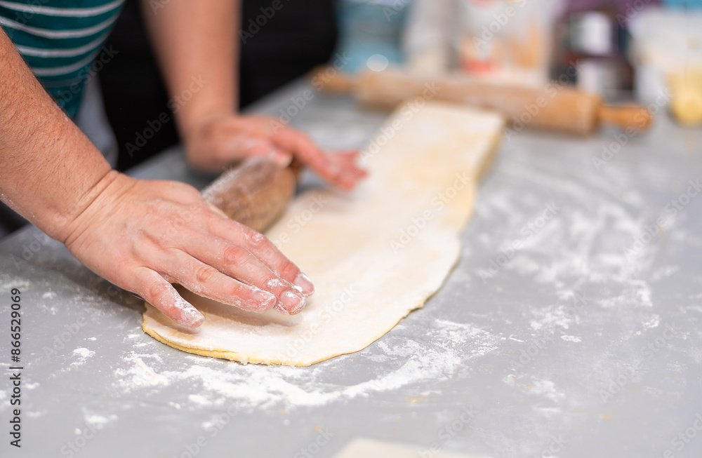 Close-up detail of unrecognizable person kneading puff pastry dough with rolling pin. Puff pastry is a dough made with flour, water, salt and fat such as butter, margarine or lard. Close-up detail of unrecognizable person kneading puff pastry dough with rolling pin. Puff pastry is a dough made with flour, water, salt and fat such as butter, margarine or lard.