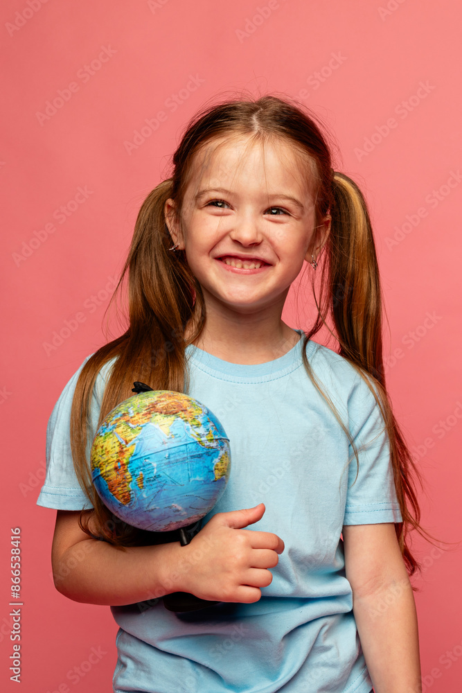 Happy smiling little schoolgirl girl in a blue t-shirt and denim shorts on a pink background with a globe in her hands. Copy space. Back to school concept. Earth Day Happy smiling little schoolgirl girl in a blue t-shirt and denim shorts on a pink background with a globe in her hands. Copy space. Back to school concept. Earth Day