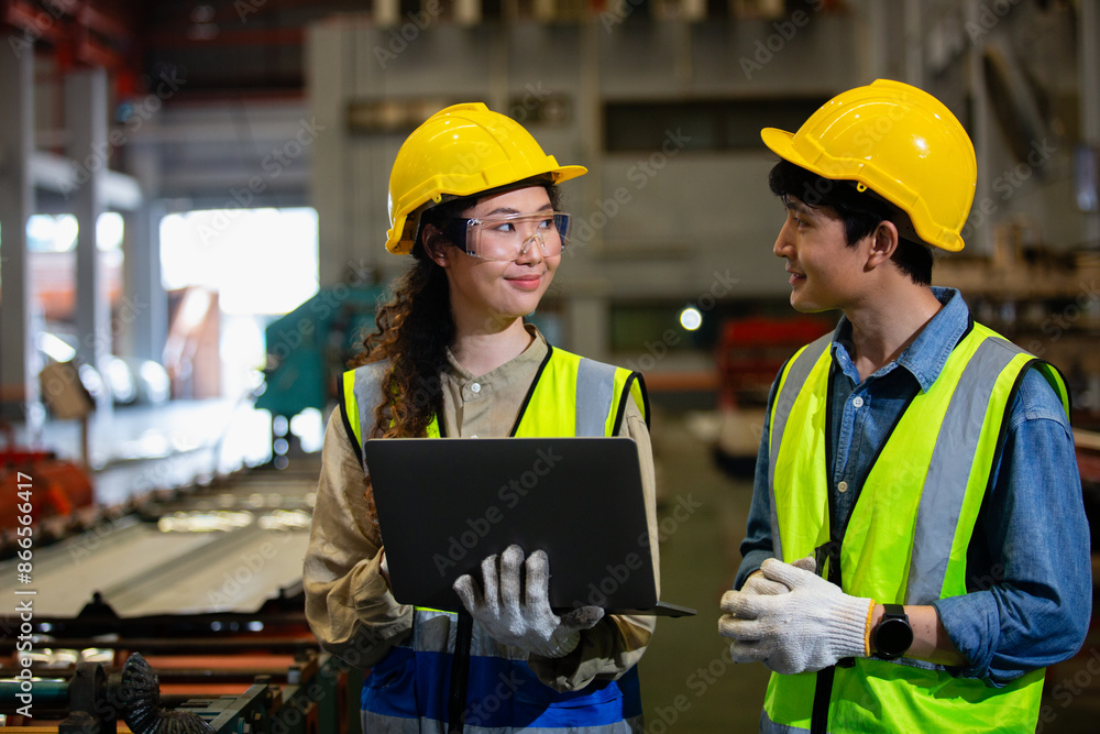 man and woman industrial engineers wear hard hats and uniform using laptop talking project of factory inside heavy industry manufacturing. Supervisor teaching work to employee. man and woman industrial engineers wear hard hats and uniform using laptop talking project of factory inside heavy industry manufacturing. Supervisor teaching work to employee.