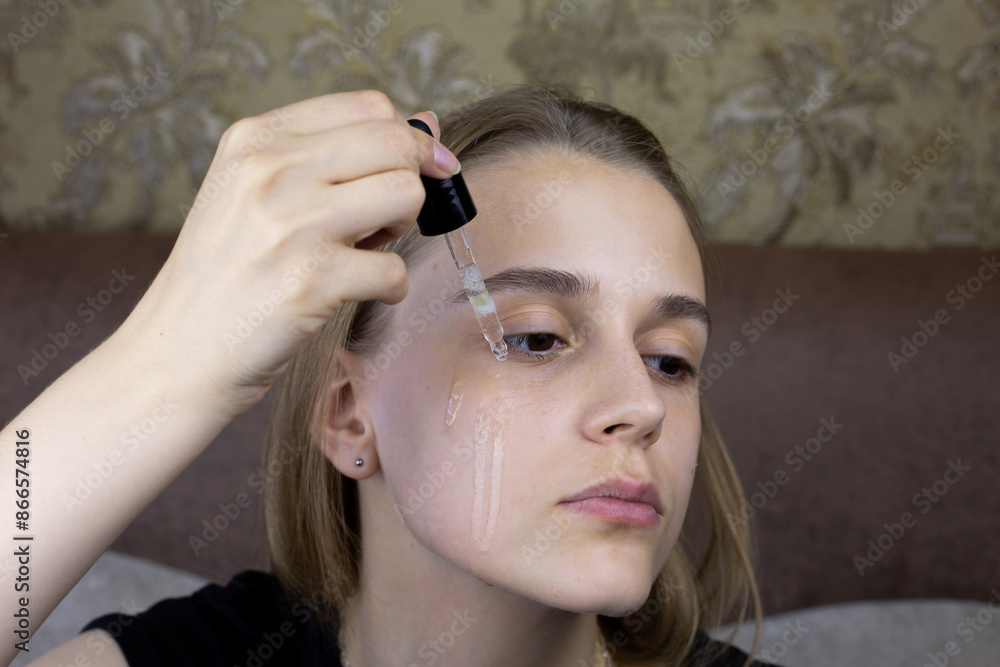 Fototapeta premium Girl is dripping special massage oil for skin care onto her face