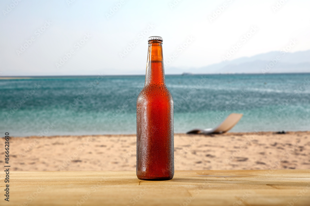 Glass bottle of cold beer and ice on wooden plank on sandy shore of a beach with copy space Glass bottle of cold beer and ice on wooden plank on sandy shore of a beach with copy space