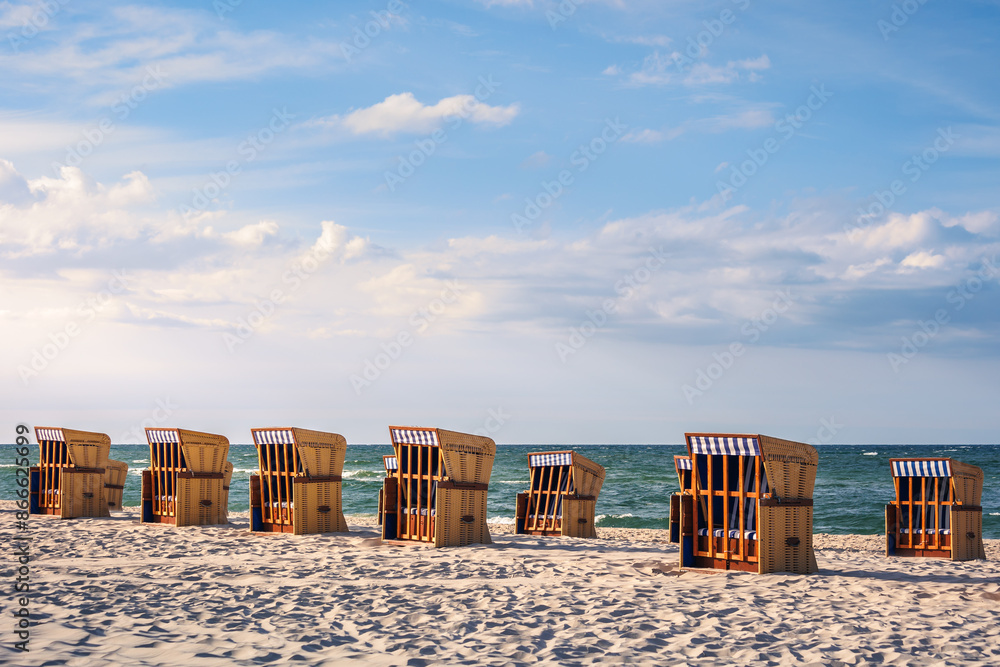 Fototapeta premium A beautiful beach basket chairs standing on the beach iluminated by sunset rays with the sea in the background