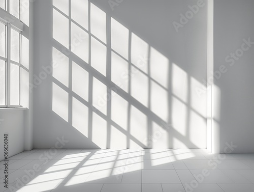 Sunlight streams through large windows, casting geometric shadows on a pristine white wall and tiled floor.