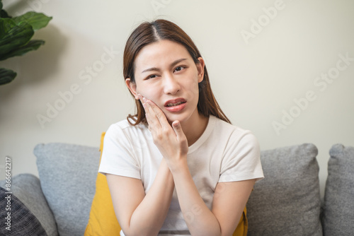 Face expression suffering from sensitive teeth, Asian young woman touching cheek photo