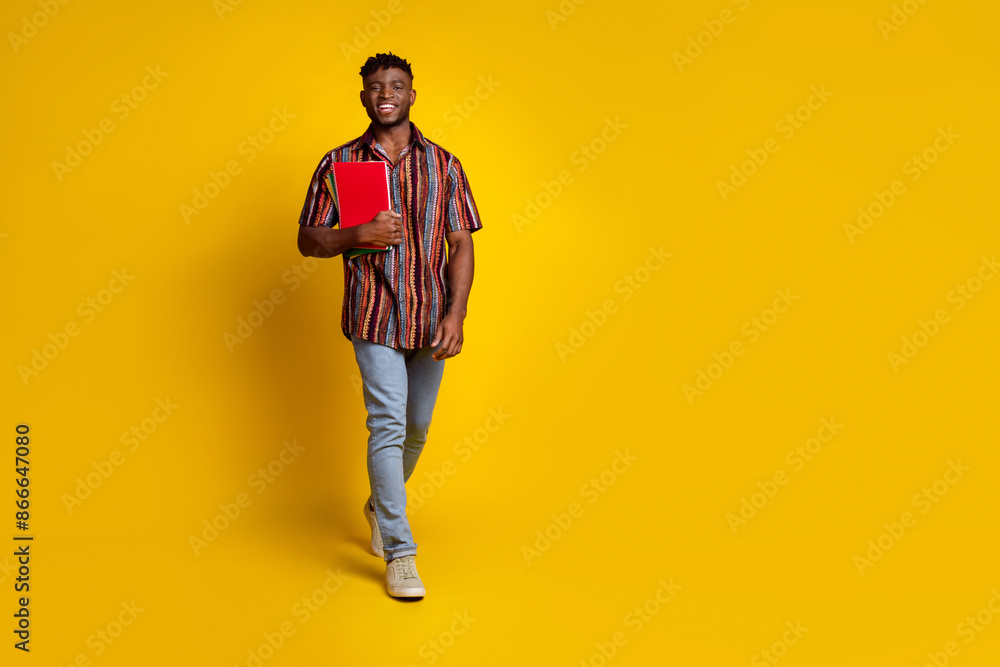 Full size photo of nice young man hold book walk empty space wear shirt isolated on yellow color background Full size photo of nice young man hold book walk empty space wear shirt isolated on yellow color background