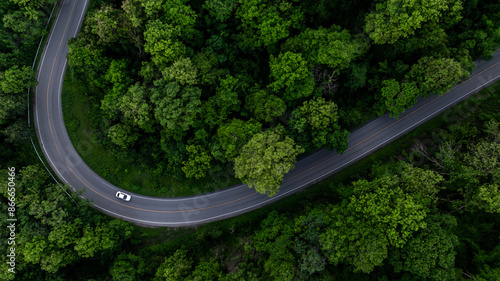 Fototapeta Naklejka Na Ścianę i Meble -  Aerial view electric vehicle car driving on asphalt road in mountain green forest, EV car electric vehicle car on forest road green energy and eco power, White electric car driving green forest road.