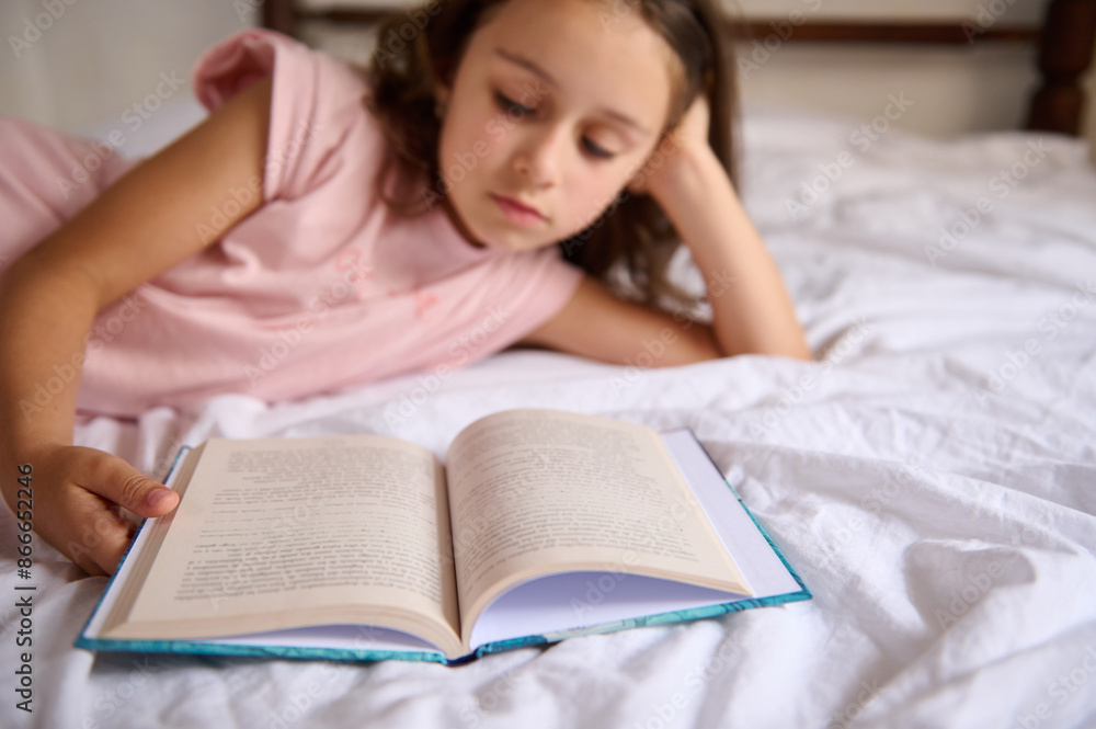 Young girl reading a book while lying on a bed Young girl reading a book while lying on a bed