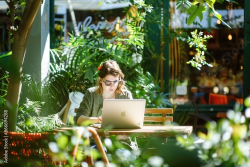 A person is using a laptop in a tranquil outdoor cafe surrounded by plants, bathed in natural sunlight AIG58 photo