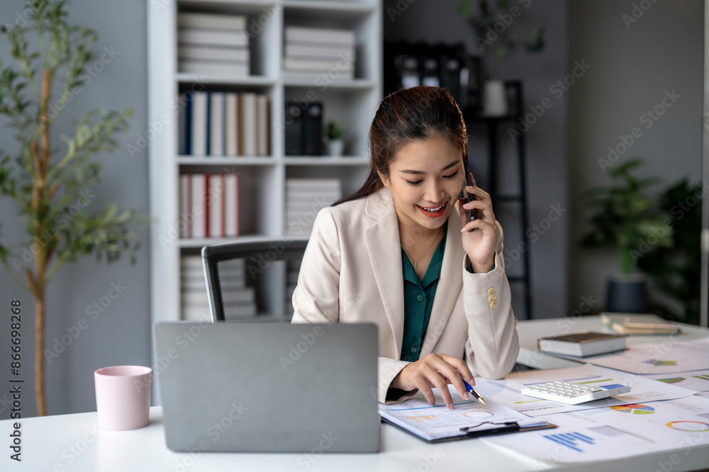 A woman is talking on her cell phone while sitting at a desk with a laptop A woman is talking on her cell phone while sitting at a desk with a laptop