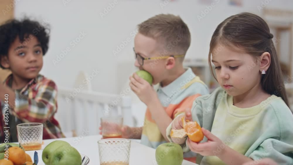 Medium of preschool multiethnic children spending time at kindergarten, eating apples, peeling tangerines and drinking juice during midday fruit time Medium of preschool multiethnic children spending time at kindergarten, eating apples, peeling tangerines and drinking juice during midday fruit time