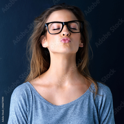 Glasses, teenager girl and blowing kiss with fashion, flirty attitude and optometry for vision in studio. Lips, pout and gen z or young woman with eyewear frame, romance and love by dark background