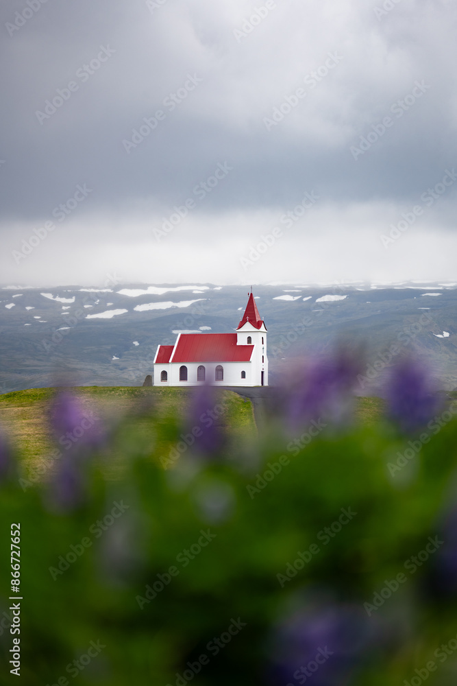 Stunning view of the Ingjaldshólskirkja, a historic little red-roofed church located in Snæfellsnes penisula, A nice road leads down and back up a hill with great views of the mountains.