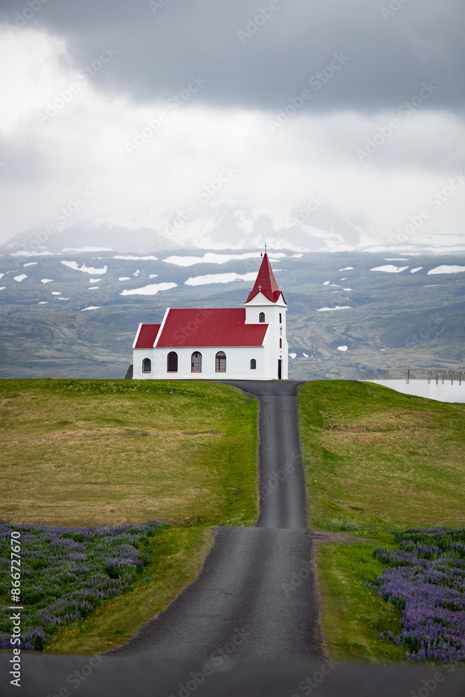 Stunning view of the Ingjaldshólskirkja, a historic little red-roofed church located in Snæfellsnes penisula, A nice road leads down and back up a hill with great views of the mountains.
