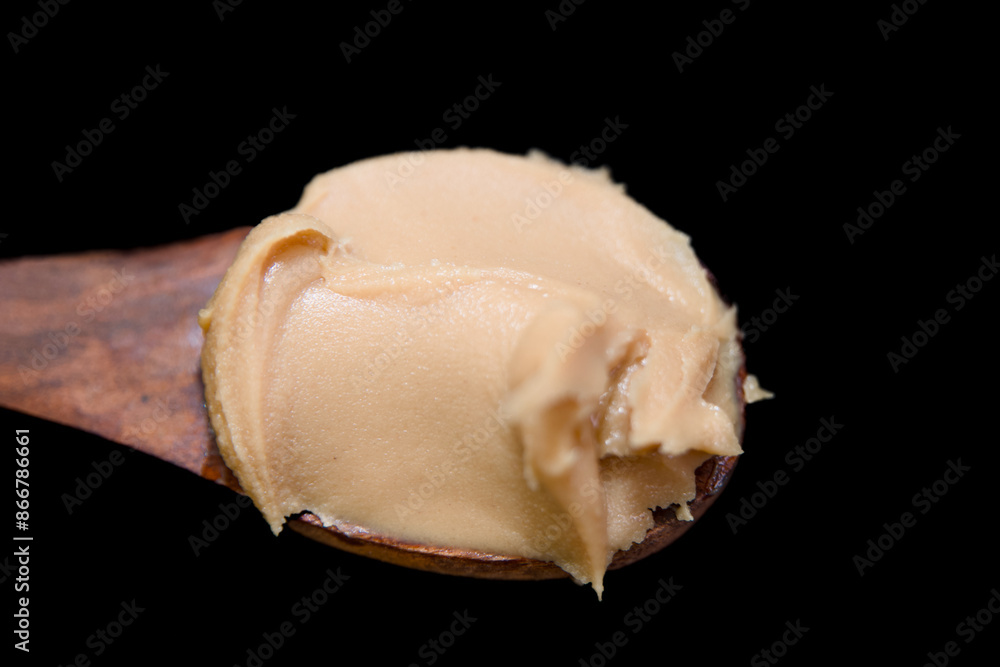 Naklejka premium Peanut butter on a wooden spoon on a black background close up