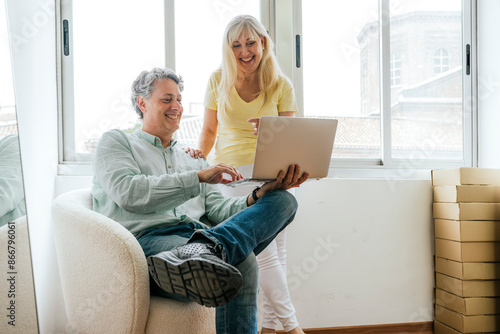 Smiling mature couple using laptop in bright room photo