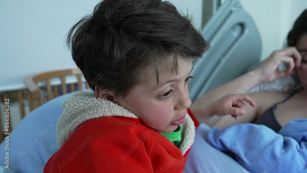 Mother breastfeeding newborn while her older son in a red hoodie gazes on in the distance with pensive expression, capturing the essence of sibling bonding and maternal care in a hospital setting Mother breastfeeding newborn while her older son in a red hoodie gazes on in the distance with pensive expression, capturing the essence of sibling bonding and maternal care in a hospital setting