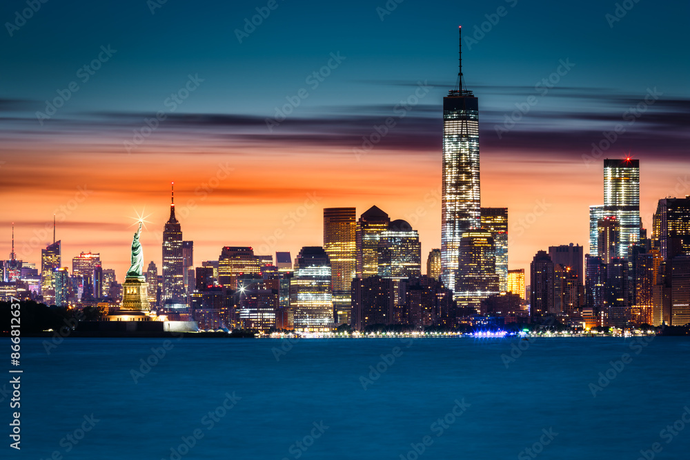 Obraz premium Sunrise over New York City with the Statue of Liberty illuminated in front of the Manhattan skyline.