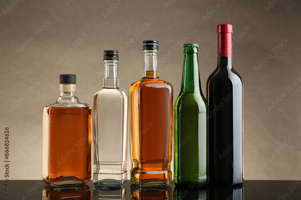 Bottles with different alcoholic drinks on table against beige background Bottles with different alcoholic drinks on table against beige background