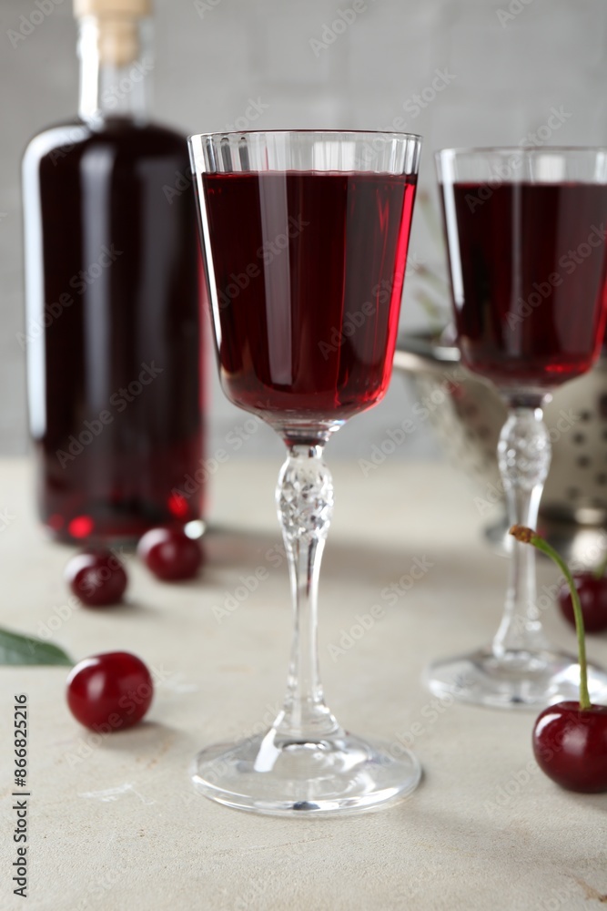 Delicious cherry liqueur in glasses, fresh berries and bottle on light grey table Delicious cherry liqueur in glasses, fresh berries and bottle on light grey table