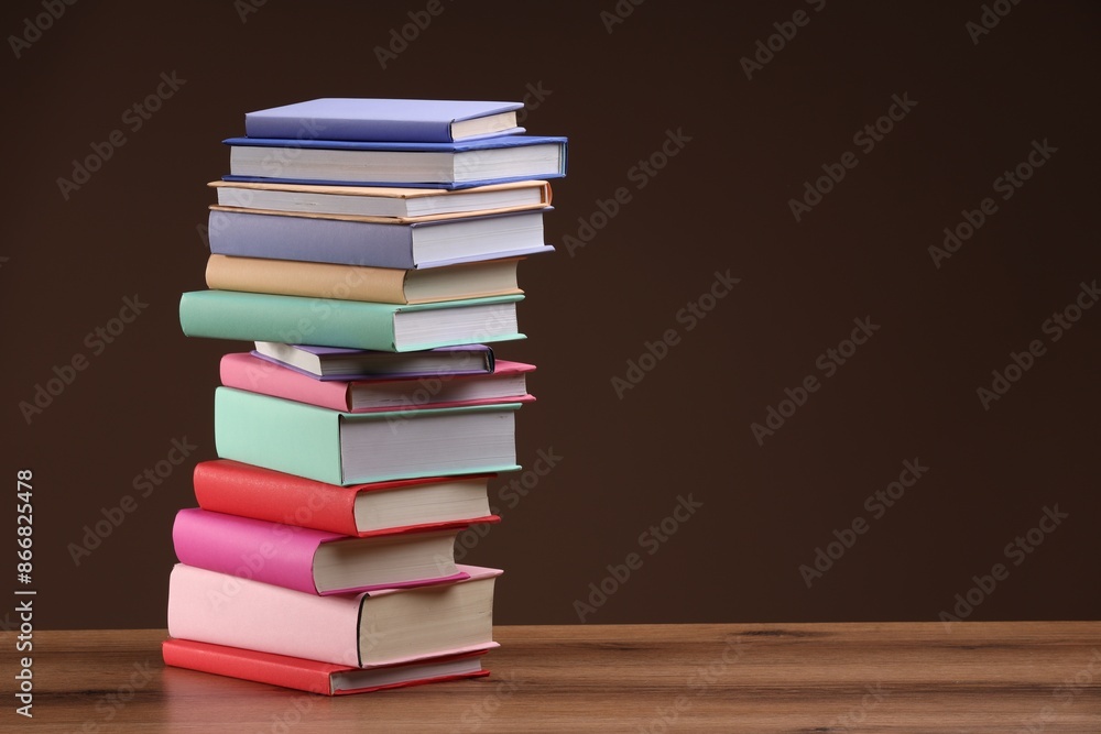Stack of colorful books on wooden table against light brown background, space for text Stack of colorful books on wooden table against light brown background, space for text