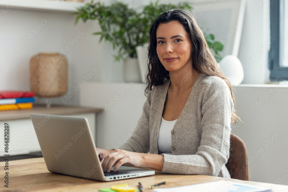 Beautiful business woman working while typing with laptop while looking at camera on a desk in the office at home. Beautiful business woman working while typing with laptop while looking at camera on a desk in the office at home.