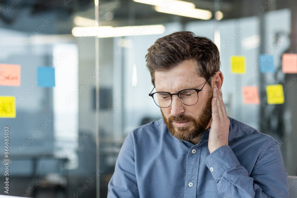 Naklejka premium Businessman experiencing discomfort at work, holding his ear in pain