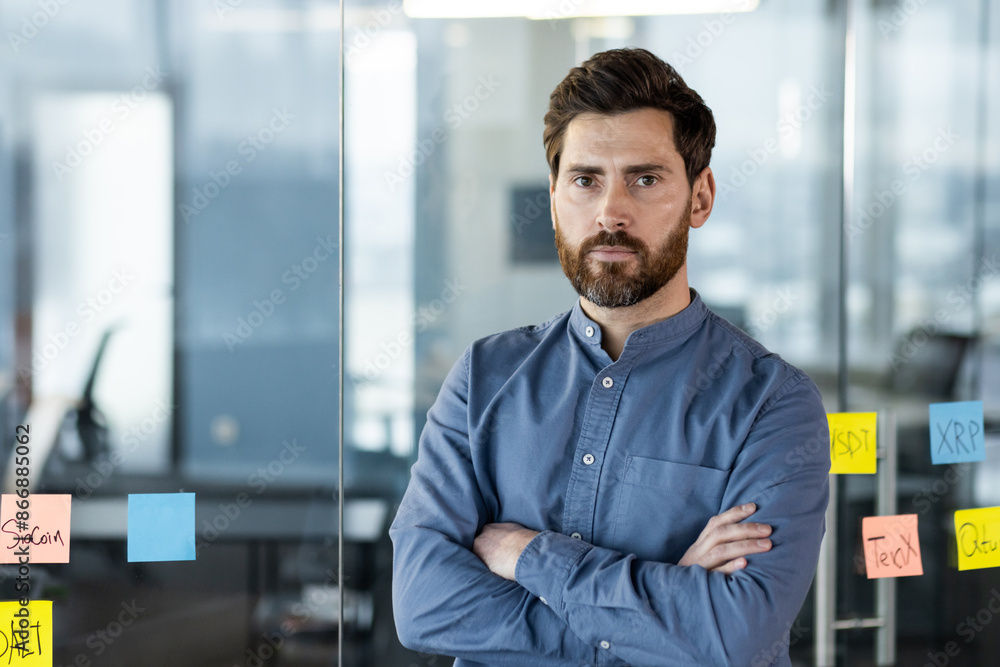 Confident businessman standing with arms crossed in modern office Confident businessman standing with arms crossed in modern office