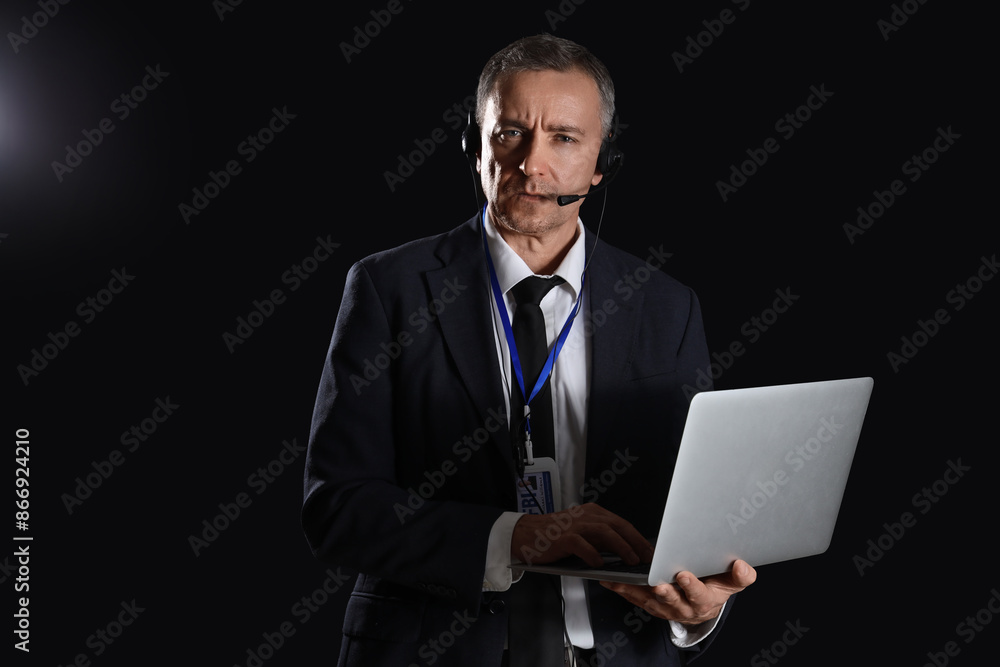 Mature FBI agent in headset using laptop on black background Mature FBI agent in headset using laptop on black background