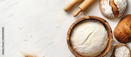 Fresh yeast dough in a bowl with flour, rolling pin, and sourdough bread on a white surface from above, with space for text. Concept of baking, pastry, and kneading.