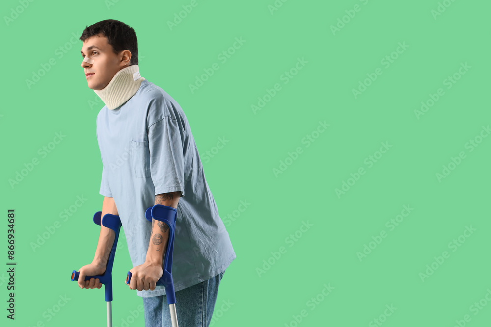 Fototapeta premium Injured young man after accident with crutches on green background
