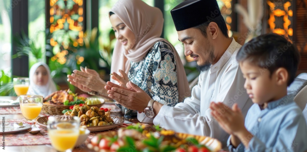 A family of four is sitting at a table, eating and praying. The man is wearing a turban and the woman is wearing a scarf. The children are sitting on chairs and the table is filled with food A family of four is sitting at a table, eating and praying. The man is wearing a turban and the woman is wearing a scarf. The children are sitting on chairs and the table is filled with food