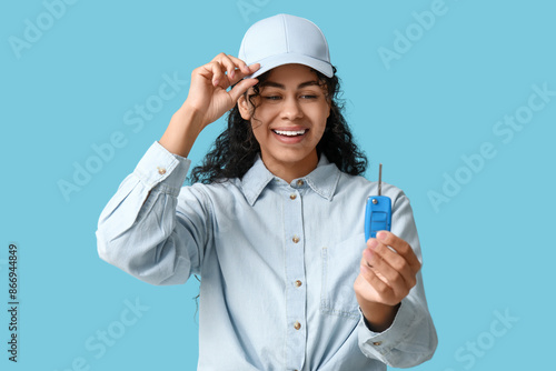 Beautiful young African-American woman with car key on blue background