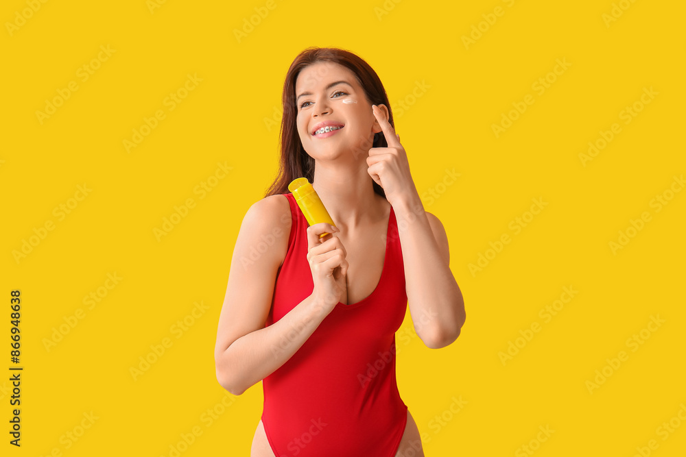 Young woman applying sunscreen cream on her face on yellow background Young woman applying sunscreen cream on her face on yellow background