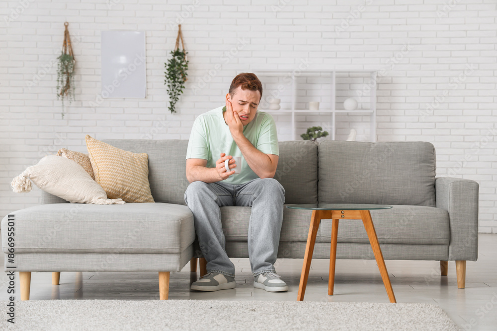 Obraz premium Young man with cup suffering from toothache in room