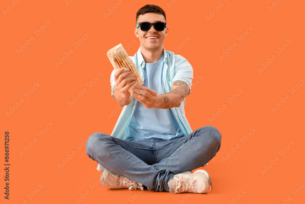 Happy young man with tasty doner kebab sitting on orange background Happy young man with tasty doner kebab sitting on orange background