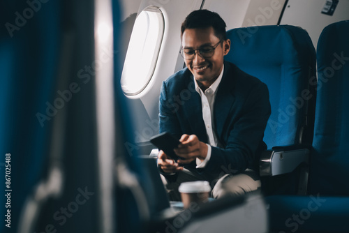 Attractive Asian male passenger of airplane sitting in comfortable seat while working laptop and tablet with mock up area using wireless connection. Travel in style, work with grace. photo