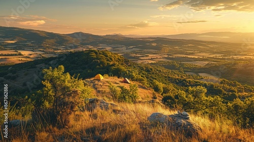 A scenic campsite on a hilltop overlooking a sprawling valley bathed in the golden light of the setting sun.