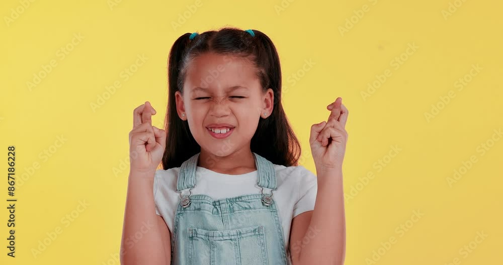 Fingers crossed, wish and child in studio with eyes closed for hope, trust and praying for good news. Smile, emoji hands and girl kid with luck, optimism or faith gesture by yellow background. Fingers crossed, wish and child in studio with eyes closed for hope, trust and praying for good news. Smile, emoji hands and girl kid with luck, optimism or faith gesture by yellow background.