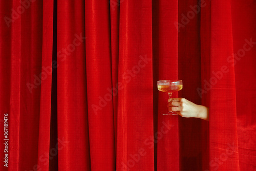 Hand holding a champagne against red velvet curtains photo