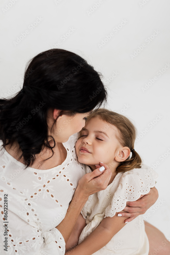 Family relationship between mother and daughter. Loving mother with her little daughter on a light studio background. Tender moment, family support. Family relationship between mother and daughter. Loving mother with her little daughter on a light studio background. Tender moment, family support.